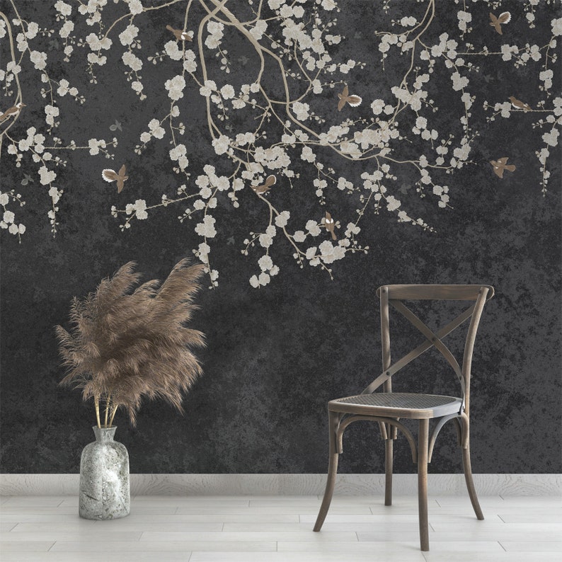 May include: A dark gray wall with a white floral design and a brown wooden chair. A vase with dried pampas grass sits on the floor in front of the wall.