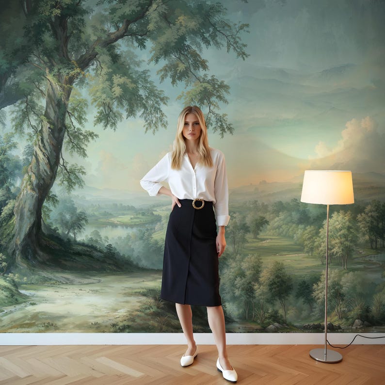 May include: A woman wearing a white button-down shirt and a black skirt with a gold belt stands in front of a large landscape painting. The painting features a large tree, a river, and rolling hills.