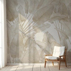 May include: A room with a large-scale wallpaper featuring a pattern of oversized, light beige banana leaves. A wooden chair with a white cushion sits in front of the wall. The room has a wooden floor and a window with white curtains.