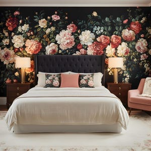 May include: A bedroom with a floral wallpaper backdrop featuring large pink, red, and white flowers. A bed with a tufted headboard, white bedding, and decorative pillows is centered. Two bedside tables with lamps flank the bed. A pink armchair and a rug complete the scene.