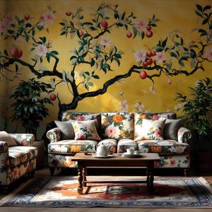 May include: A living room with a floral patterned couch, two armchairs, a coffee table, and a bookcase. The wall behind the couch is painted with a mural of a yellow tree with pink flowers and red apples.