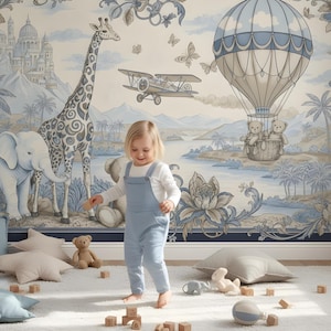 Pode incluir: Uma cena de ber&ccedil;&aacute;rio caprichosa com uma crian&ccedil;a de macac&atilde;o azul em frente a um mural. O mural retrata uma girafa, um elefante, um bal&atilde;o de ar quente com ursinhos de pel&uacute;cia e um avi&atilde;o, todos em tons suaves de azul e bege. Almofadas e brinquedos est&atilde;o espalhados em um tapete branco.