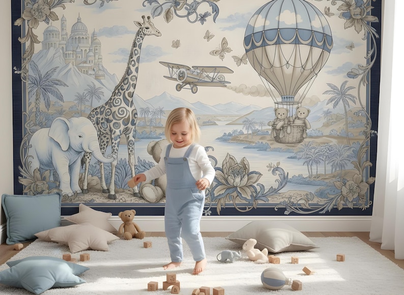 Pode incluir: Uma cena de ber&ccedil;&aacute;rio caprichosa com uma crian&ccedil;a de macac&atilde;o azul em frente a um mural. O mural retrata uma girafa, um elefante, um bal&atilde;o de ar quente com ursinhos de pel&uacute;cia e um avi&atilde;o, todos em tons suaves de azul e bege. Almofadas e brinquedos est&atilde;o espalhados em um tapete branco.
