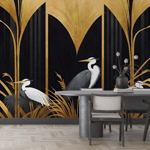 May include: A black and gold art deco style mural featuring two herons with white and gray feathers. The background is black with gold stylized plants and geometric shapes. A gray table and chairs are in the foreground.