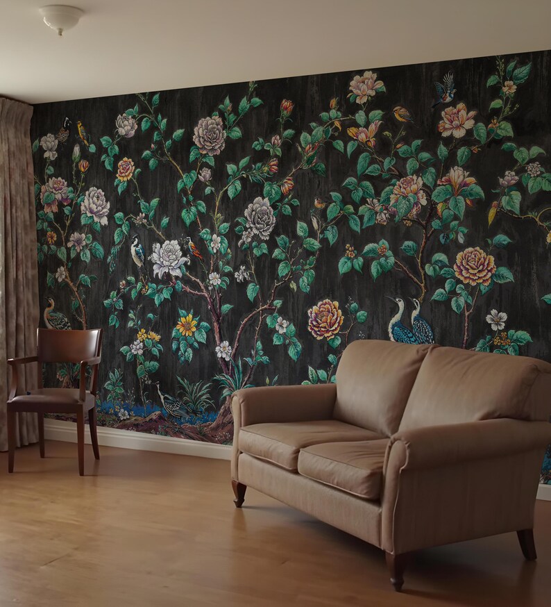 May include: A room with a dark floral wallpaper featuring roses, birds, and foliage. A brown leather sofa and a wooden chair are positioned in front of the wallpaper. The room has wooden flooring and curtains.