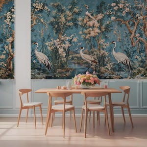 Op de afbeelding: Een eetkamer met een muurschildering met een blauwe achtergrond met witte kranen en bloeiende bloemen. Een houten tafel met zes stoelen is gedekt met een vaas met roze bloemen en andere decoratieve items.