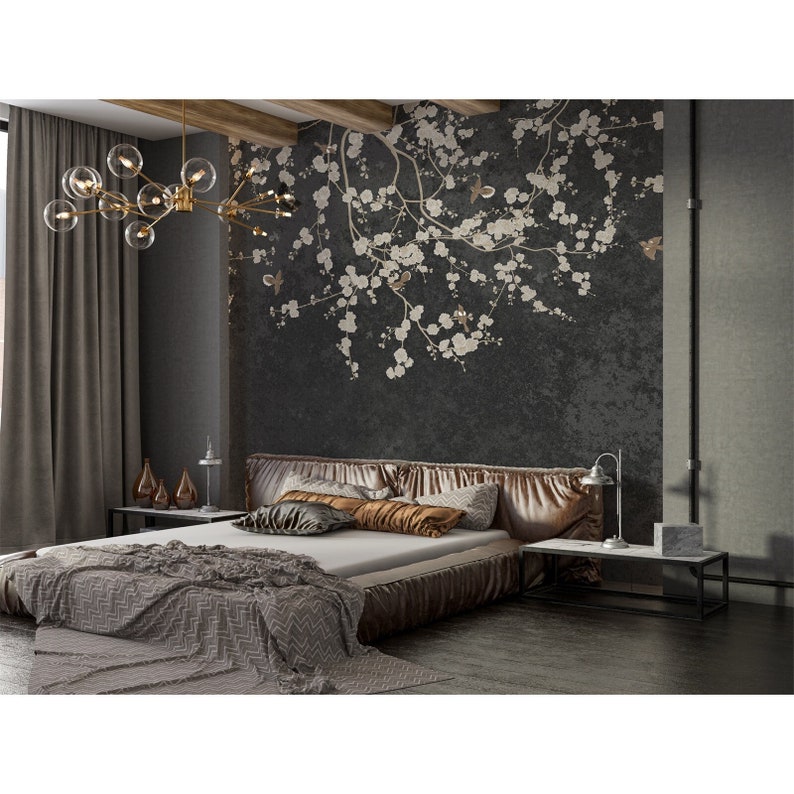 May include: A bedroom with a dark gray wall featuring a white floral wallpaper design. A bed with a brown headboard and a gray and white blanket is in the center of the room. A gold chandelier hangs above the bed.