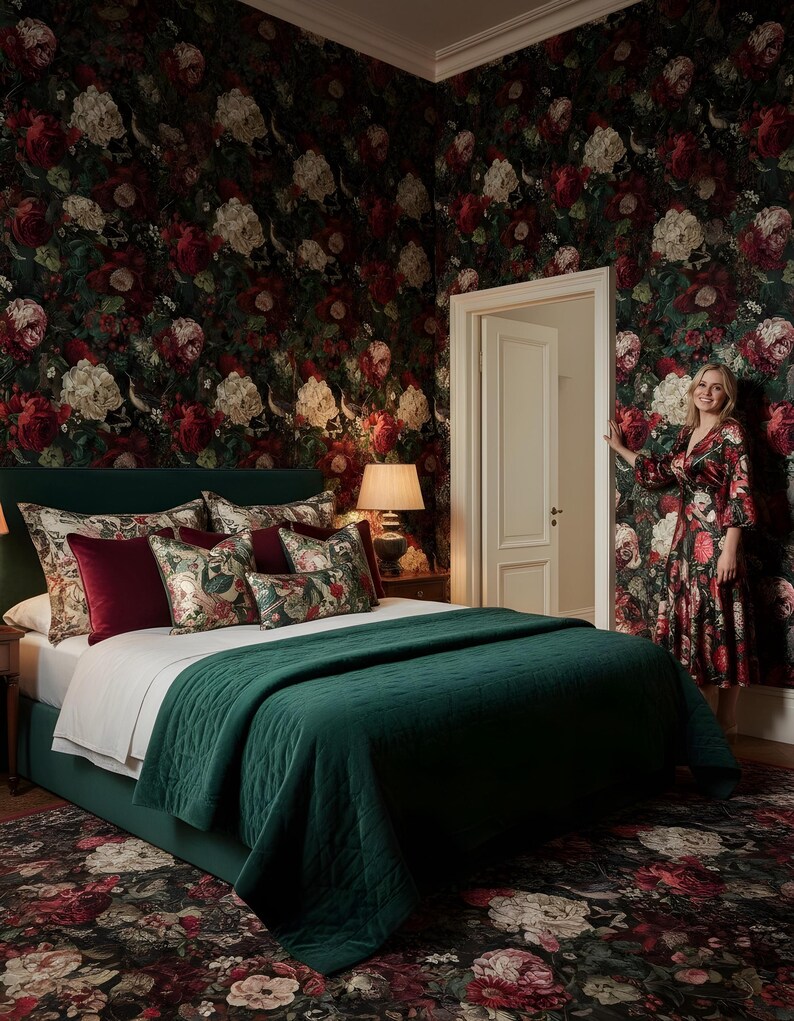 May include: A bedroom with a dark green bed, a matching quilt, and floral patterned pillows. The walls are covered in a dark floral wallpaper. A woman in a floral dress stands in the doorway.