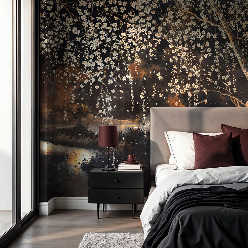 May include: A bedroom with a dark floral wallpaper featuring white blossoms and a river scene. A black nightstand with a burgundy lamp and pillows complements the bed. The room has a modern, elegant aesthetic.