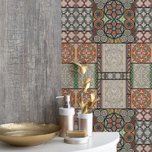 May include: A bathroom with a gray wood-look wall and a patterned tile backsplash. The backsplash features a variety of geometric designs in shades of red, blue, green, and yellow. A gold metal bowl sits on a white countertop in front of the backsplash. Two gold soap dispensers and a bar of soap are also on the countertop.