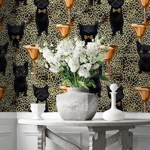 May include: A gray console table with a black and gold wallpaper featuring a repeating pattern of black cats wearing bow ties and martini glasses. White flowers are in a gray ceramic vase on the table.
