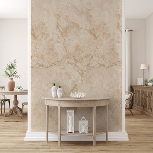 Op de afbeelding: Een lichte houten consoletafel met een gebogen bovenblad en een onderplank. De tafel is versierd met witte keramische vazen, een wit decoratief object en twee witte lantaarns. De tafel staat voor een muur met een beige marmerpatroon.