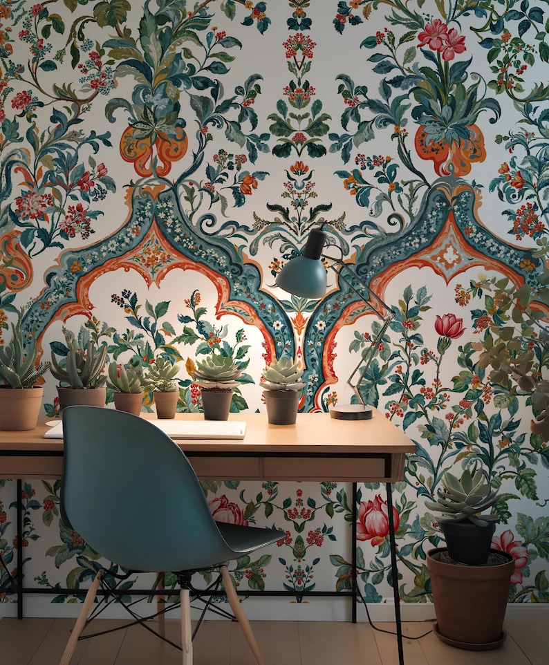 Op de afbeelding: Een thuiskantoor met een houten bureau, een turquoise stoel en een turquoise bureaulamp. Het bureau heeft potplanten en een laptop. De achtergrond is bloemenbehang met een witte basis en ingewikkelde patronen in turquoise, oranje en groen.