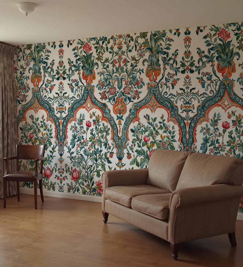 Op de afbeelding: Een kamer met bloemenbehang in cr&egrave;me, rood, groen en oranje. Een bruine leren bank en een houten stoel staan in de kamer. Het behang heeft een herhalend bloemenpatroon.