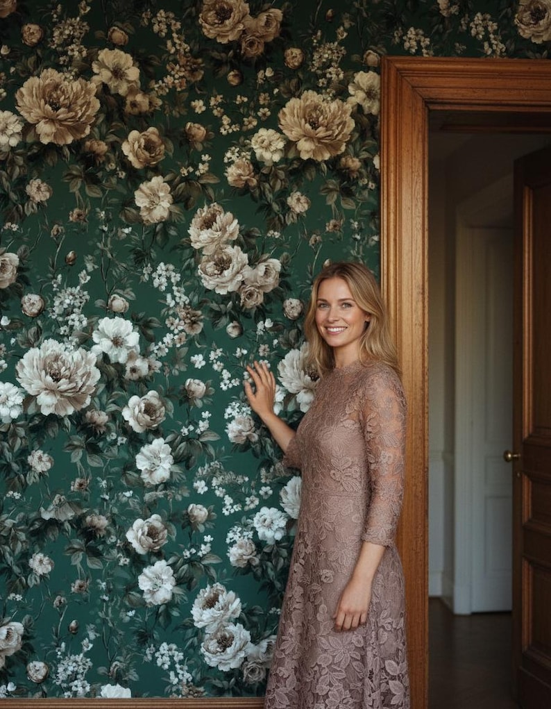 May include: A woman in a mauve lace dress stands near a wall covered in dark green floral wallpaper. The wallpaper features large, cream-colored peony and rose blooms. A wooden door frame is visible on the right side of the image.