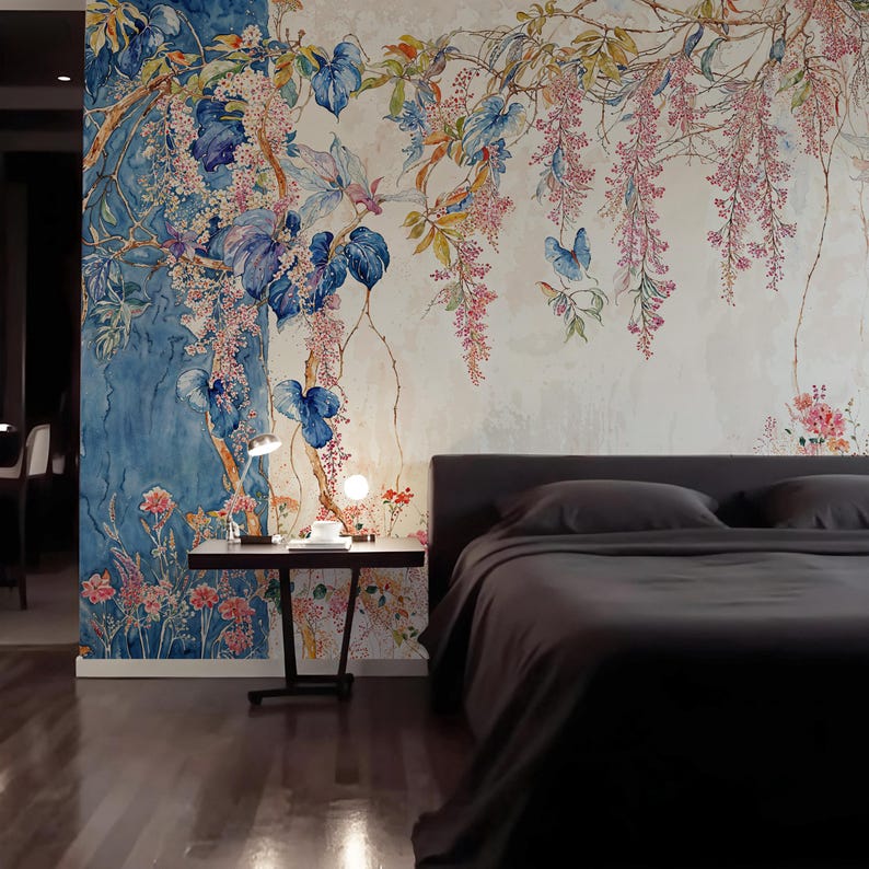 May include: A bedroom with a floral mural featuring blue, pink, and green botanical elements. The mural covers the wall behind a bed with dark gray bedding. A small black side table with a lamp and decor sits next to the bed.