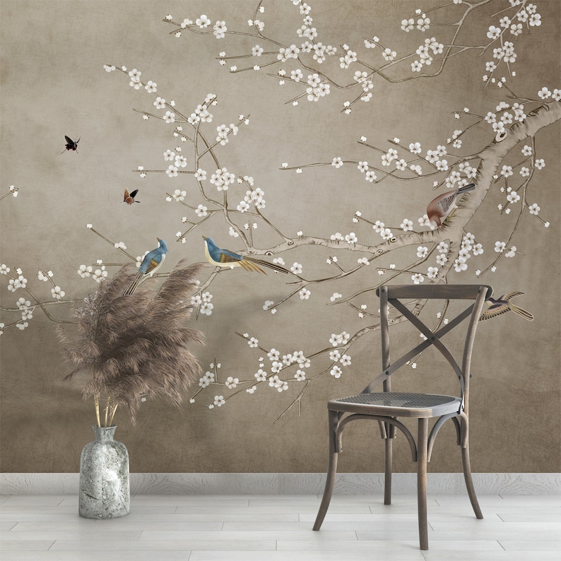 May include: A brown wooden chair with a cross-back design sits in front of a wall with a floral wallpaper featuring a delicate branch of white blossoms and blue birds.