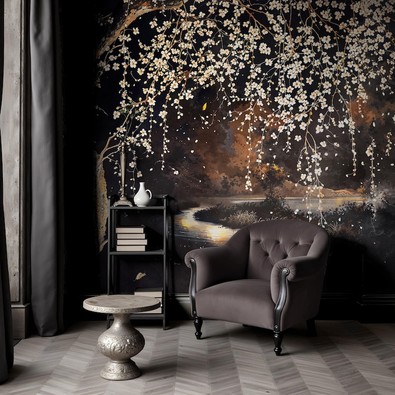 May include: A room with a dark floral mural featuring a tree with white blossoms. A gray velvet armchair, a small silver table, and a black metal shelf with books and a vase are in front of the mural. The floor has a gray and white herringbone pattern.