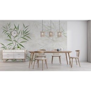 Op de afbeelding: Een lichte houten eettafel met vier stoelen en drie hanglampen. De muur achter de tafel heeft een groen-witte bamboe behang.