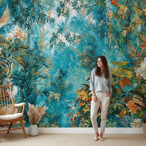 May include: A teal blue and green floral wallpaper mural with a woman standing in front of it. The mural features a variety of flowers, leaves, and birds. The woman is wearing a light blue shirt and white pants.