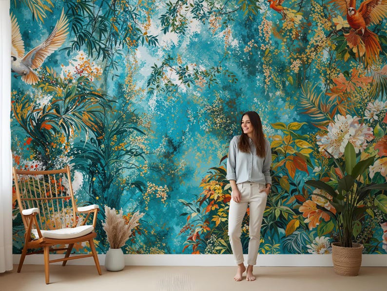 May include: A teal blue and green floral wallpaper mural with a woman standing in front of it. The mural features a variety of flowers, leaves, and birds. The woman is wearing a light blue shirt and white pants.