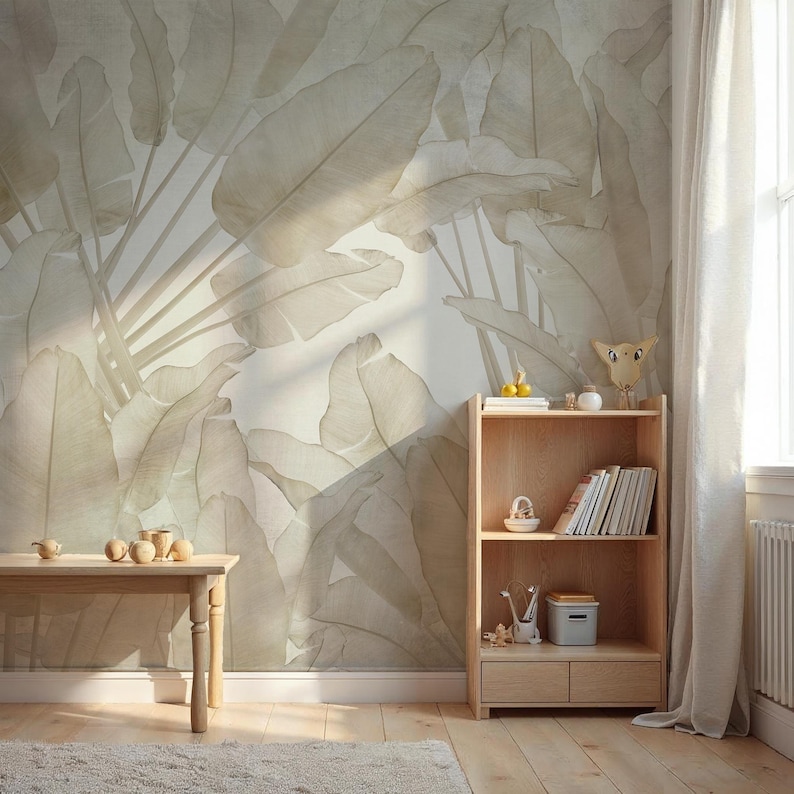 May include: A room with a large, neutral-toned banana leaf wallpaper. A light wood bookshelf and small table are in the room. The table has several small wooden decorative objects. A rug and curtain are also visible.