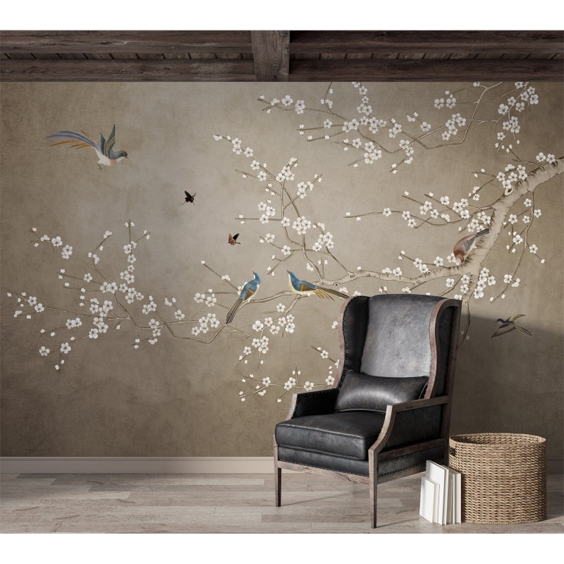 May include: A black armchair with a wingback design sits in front of a wall mural featuring a delicate branch of a flowering cherry tree with white blossoms and blue birds. The background is a light brown color.