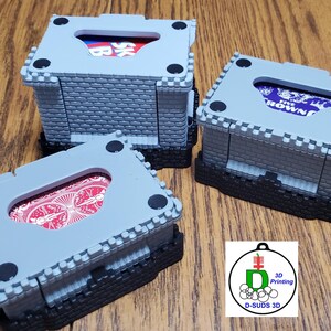 May include: Three gray and black card holders with a castle design. Each holder has a rectangular opening revealing a portion of the cards inside. The holders are on a wooden surface. The cards visible have red and blue designs.
