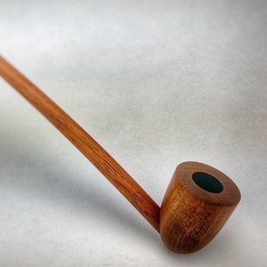 May include: A long, wooden smoking pipe with a brown finish and a black bowl. The pipe is curved and has a long stem.