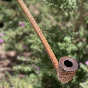 Könnte beinhalten: Eine Holzpfeife mit einem langen, schlanken Schaft und einem Kopf mit dunkelbrauner Oberfläche. Die Pfeife hat ein natürliches Holzmaserungsmuster.
