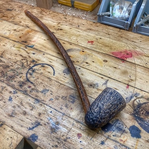 Puede incluir: Una pipa de fumar de madera con un acabado marrón y negro. La pipa está sobre una superficie de madera con muchos arañazos y marcas.