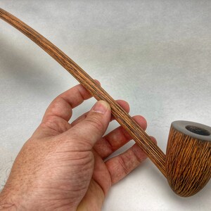 May include: A long, wooden smoking pipe with a brown and black striped finish. The pipe has a curved stem and a bowl that is slightly wider than the stem.
