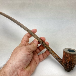 May include: A long, brown wooden smoking pipe with a curved stem and a bowl with a black interior.