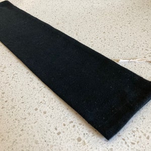 May include: A black fabric pouch with a drawstring closure. The pouch is made of a soft, textured fabric and has a simple, minimalist design.