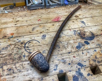 May include: A wooden smoking pipe with a dark brown finish and a bowl made of wood and a light brown material. The pipe is lying on a wooden surface with a lot of scratches and paint splatters.