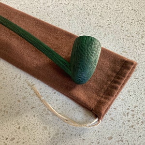 Puede incluir: Una pipa de fumar de madera verde con una bolsa de tela marrón. La pipa es larga y delgada con una cazoleta curva.