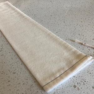 May include: A plain white drawstring pouch with a black stitching around the edges. The pouch is made of a soft, natural fabric.