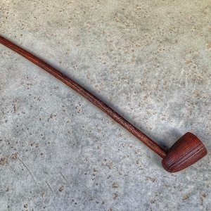 May include: A long, wooden pipe with a brown finish. The pipe has a long, thin stem and a bowl that is slightly wider than the stem.