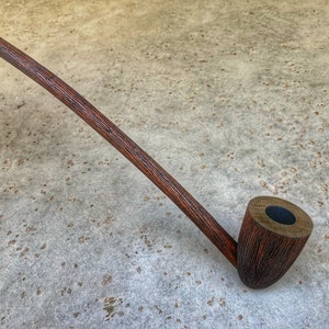 May include: A long, wooden smoking pipe with a dark brown finish. The pipe has a long, curved stem and a bowl with a black interior.