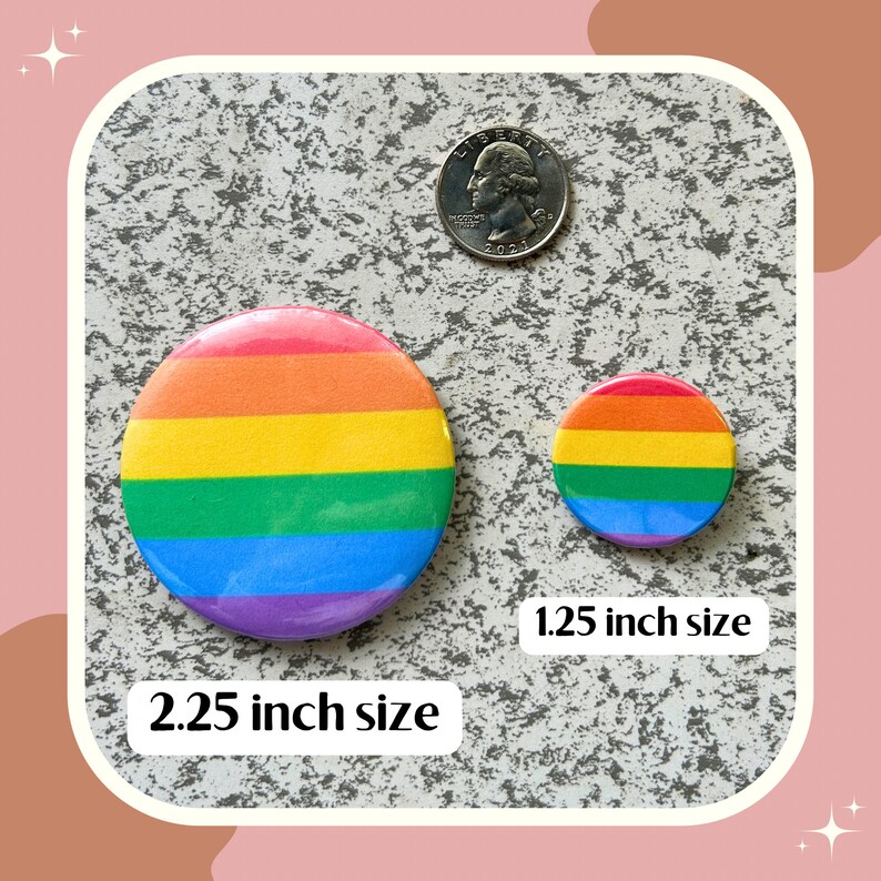 May include: Two rainbow pride buttons, one 2.25 inches and one 1.25 inches in diameter. The buttons are on a gray textured surface.