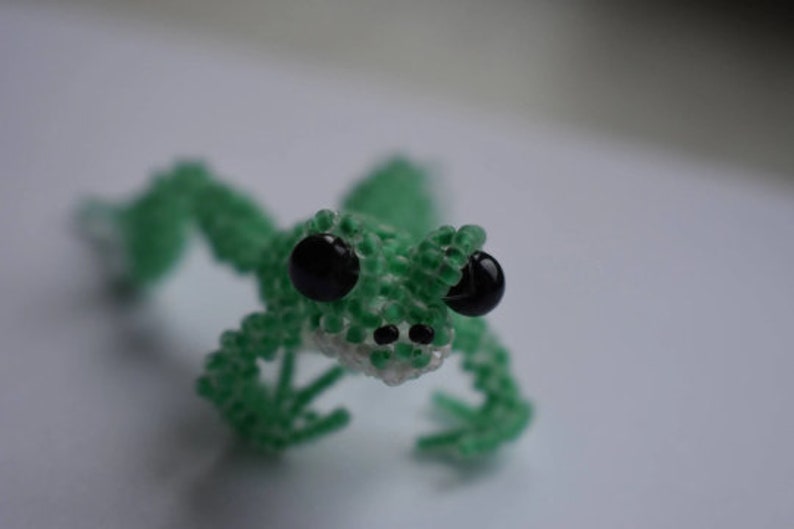 May include: A green beaded frog with black eyes. The frog is made of small green beads and has a white beaded belly.