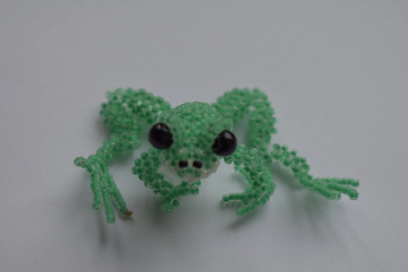 May include: A green beaded frog with black eyes. The frog is made of small green beads and has a white mouth.