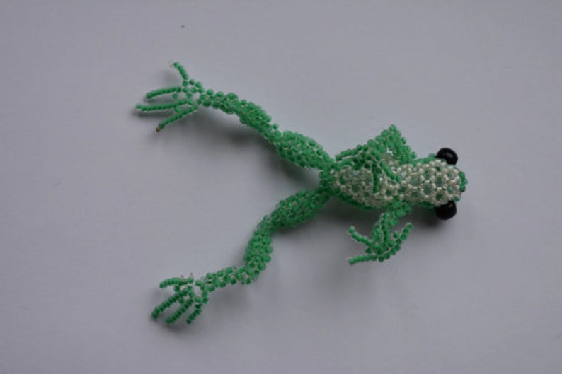 May include: A green beaded frog with black eyes. The frog is made of small green beads and has a white beaded belly.