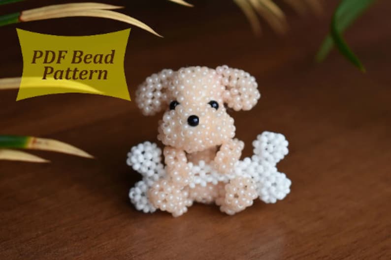 May include: A beaded dog figurine holding two white beaded bones. The dog is light pink and has black eyes. The text "PDF Bead Pattern" is in a yellow box in the upper left corner of the image.