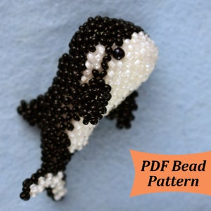 May include: A black and white beaded orca whale, a popular ocean animal, is shown in a close-up view. The orca is made with small black and white beads. The orca is posed in a swimming position. The image includes the text "PDF Bead Pattern".