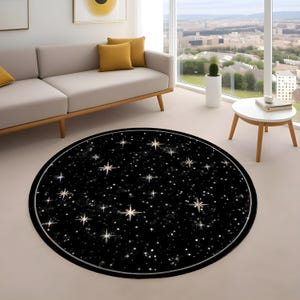 Pode incluir: Um tapete redondo preto com um design celestial. O tapete apresenta um padrão de estrelas brancas e douradas de vários tamanhos sobre um fundo preto. Uma borda prateada emoldura o tapete, que é colocado sobre um chão de cor clara.