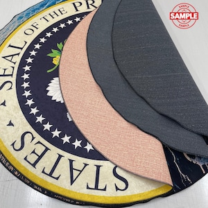 May include: Circular rug displaying the Presidential Seal in navy blue and cream. The rug has a yellow border and a black backing. The word "SAMPLE" is stamped on the rug.
