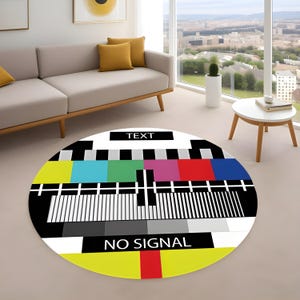 May include: A circular rug with a retro test card design. The rug displays a pattern of coloured bars and lines in black, white, yellow, blue, green, and red. The words "TEXT" and "NO SIGNAL" are printed on the rug.