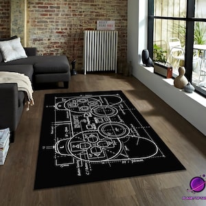 May include: Black rectangular rug with a white blueprint design of a video game controller. The rug features the word "SONY" and technical details. It is placed on a wooden floor. The rug's dimensions are approximately 70cm in height.