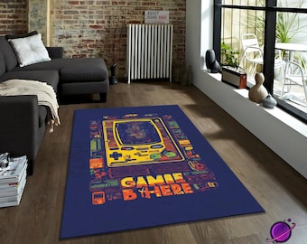 May include: A rectangular, navy blue rug featuring a retro handheld game console design in yellow, orange, and green. The words "GAME HERE" are printed in orange and red. The rug is suitable for a living room or game room.